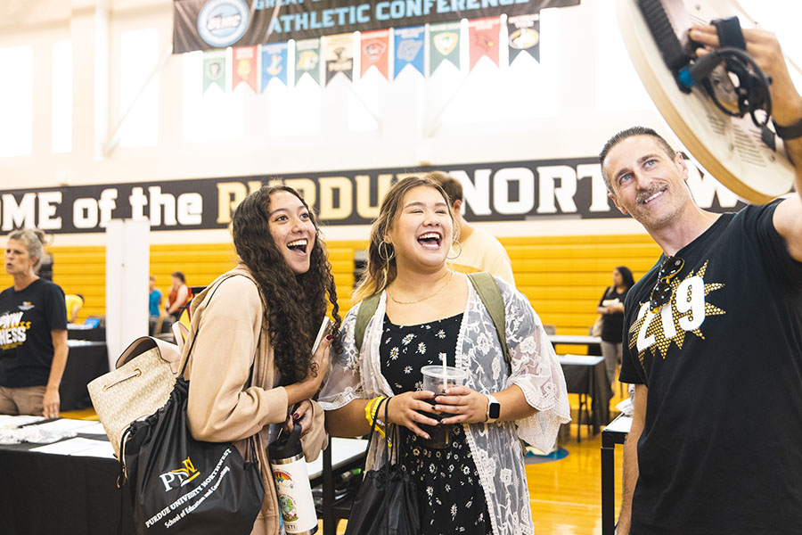 Two students smile while taking a photo with a photographer