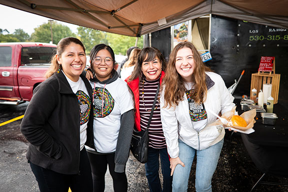 Four people lean into each other and pose. They are all smiling. Three of the people are wearing PNW's hispanic heritage month shirts while the fourth person is wearing a striped shirt.