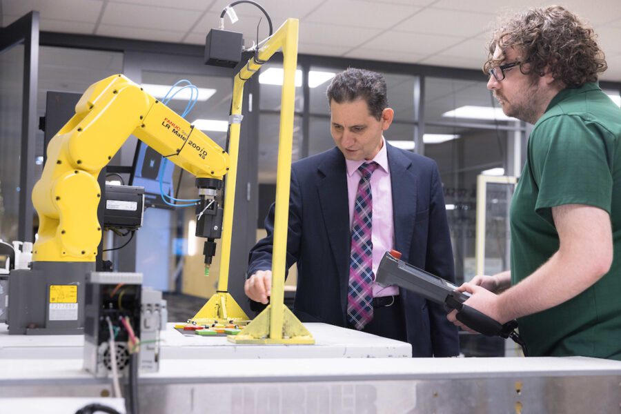 PNW Professor Maged Mikhail works with a student on a yellow mechatronics machine.