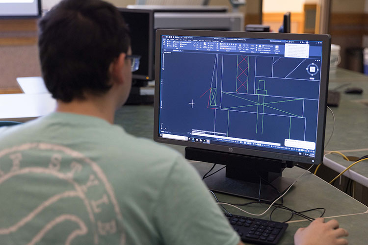 A student works on a computer during class. They have a digital building program open on their computer.