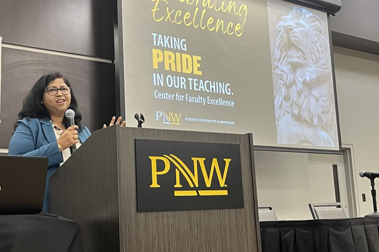 Neeti Parashar stands behind a wooden podium with the "PNW" logo on it. She is wearing a blue blazer and white shirt and talking into a microphone.