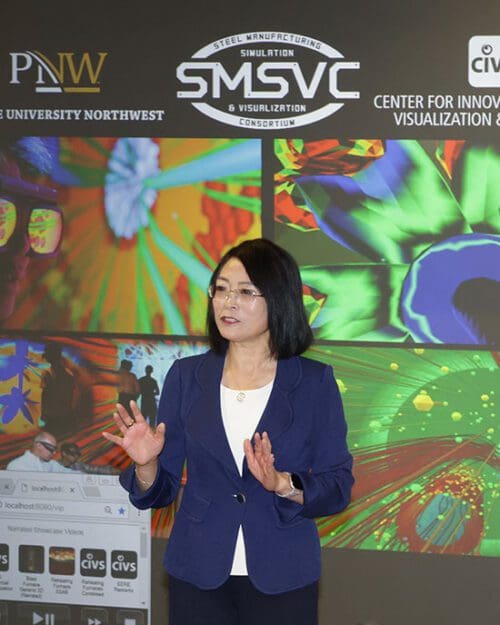 Chenn Zhou stands in front of a projection screen that shows images of blast furnace operations.