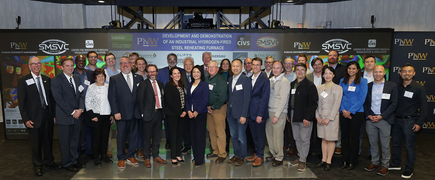 A large group of individuals in business professional attire stand together in front of a large screen.