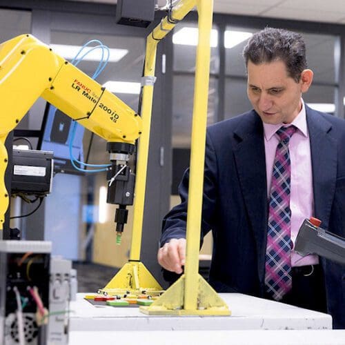 PNW Professor Maged Mikhail works with a student on a yellow mechatronics machine.