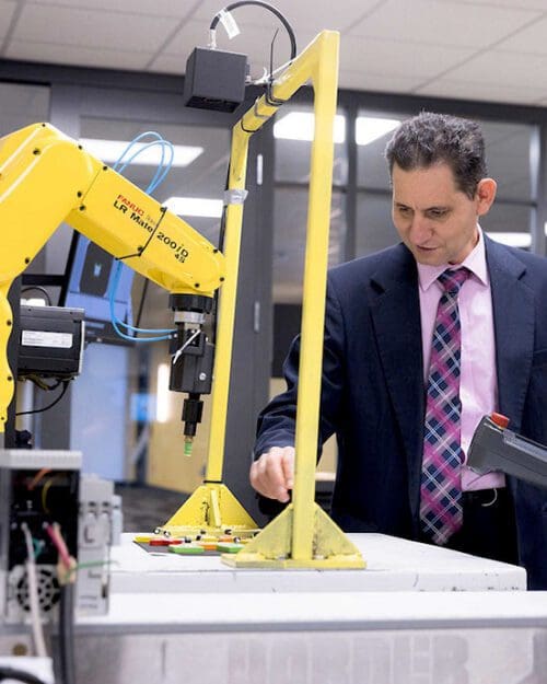 PNW Professor Maged Mikhail works with a student on a yellow mechatronics machine.