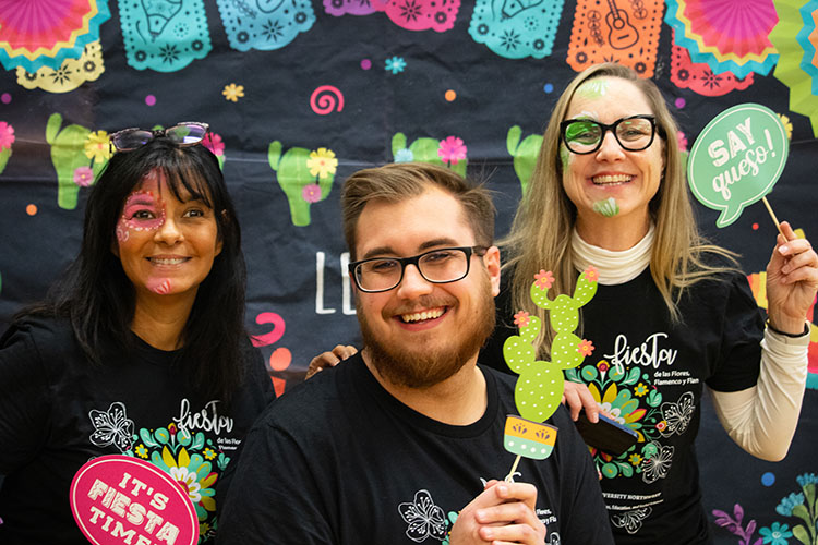 Three smiling individuals pose for photo while two wear face paint with props in celebration of Hispanic culture.