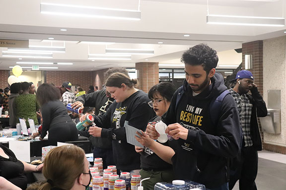 Students stand at tables that are filled with glitter and other craft supplies