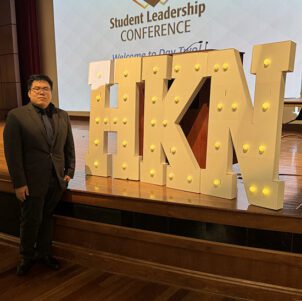 A PNW Student stands next to a marquee sign reading "HKN"