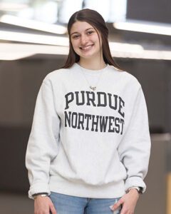 A student with long brown hair stands in DSAC. They are wearing a light gray Purdue Northwest sweatshirt