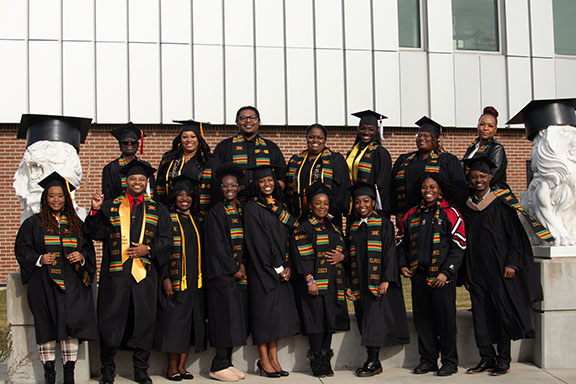 A group of graduates stand outside the Nils Building in their graduation regalia