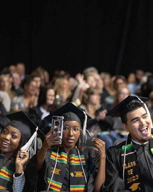 Three students pose with their phones in the air