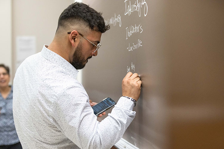 A student in a long sleeve button up writes on a brown chalk board