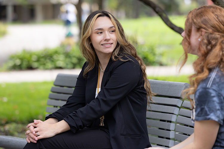 A student in a black blazer sits on a bench outside