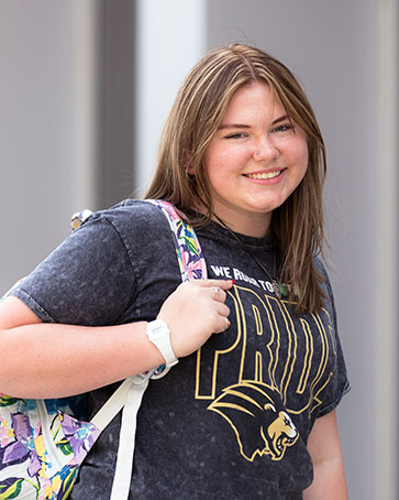 A student poses outdoors in a backpack and PNW Pride t-shirt.