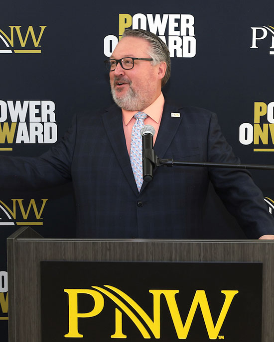 New PNW Chancellor Chris Holford speaks in front of a PNW "Power Onward" backdrop.