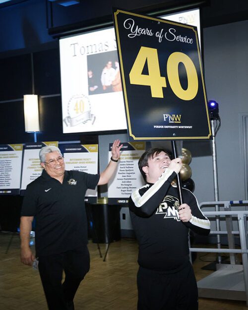 A PNW cheerleader walks in with a "40" sign to honor 40 years of service for lead service maintenance worker Tommy Sanchez at PNW Founders Day 2024.
