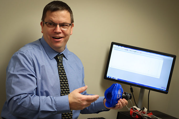 John Durocher stands by a computer and holds a piece of cardiopulmonary exercise testing equipment