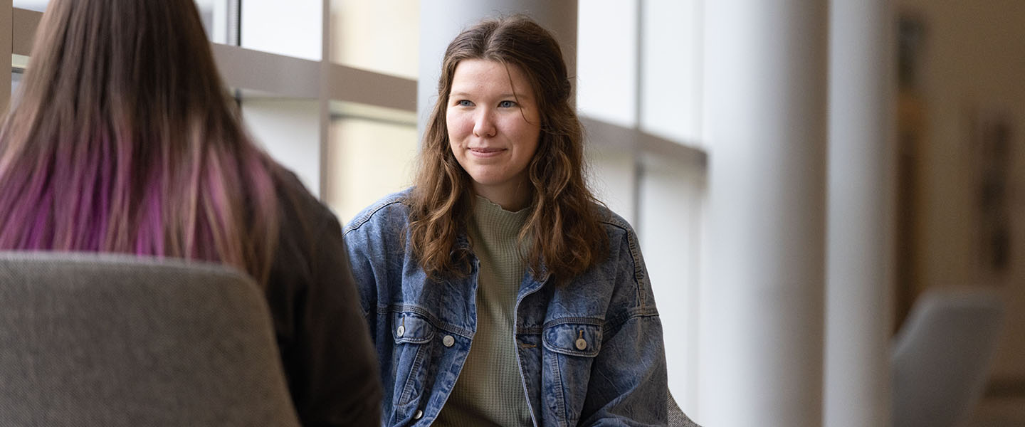 A student in a jean jacket and green shirt sits in front of windows