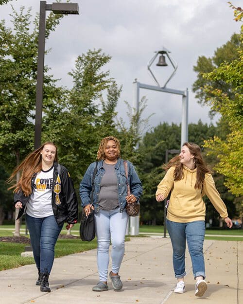 Three students walk together outside. The PNW bell tower is in the background