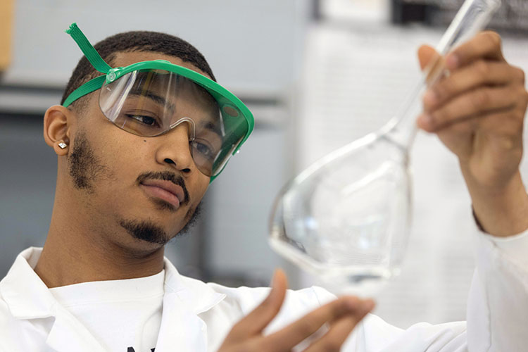A student in a lab coat inspects a flask