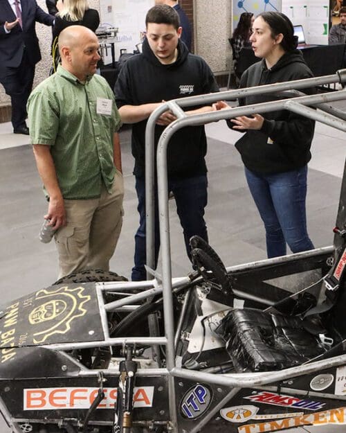 Students stand around a baja team car.