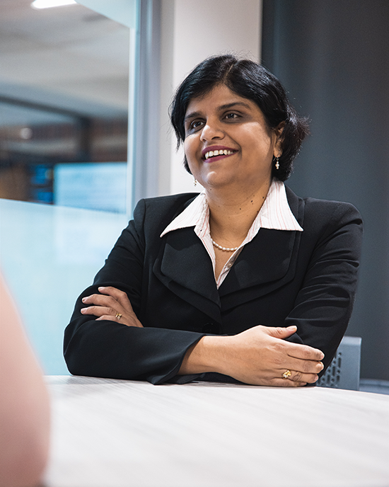 Shreya Bhandari sits at a table with her arms crossed and resting on the table.