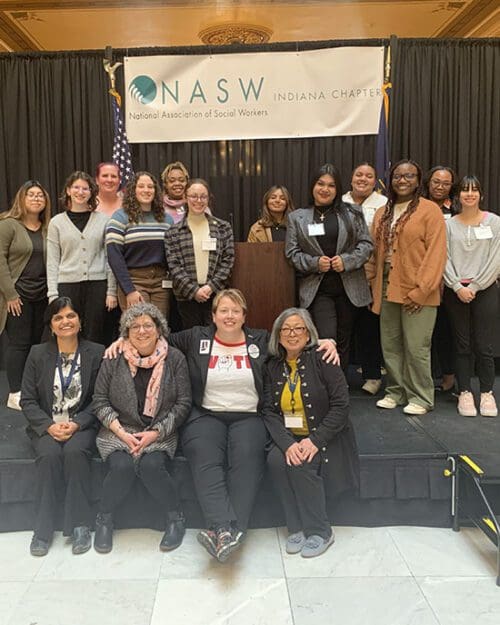 A group of students and faculty post on stage with members of the NASW leadership.