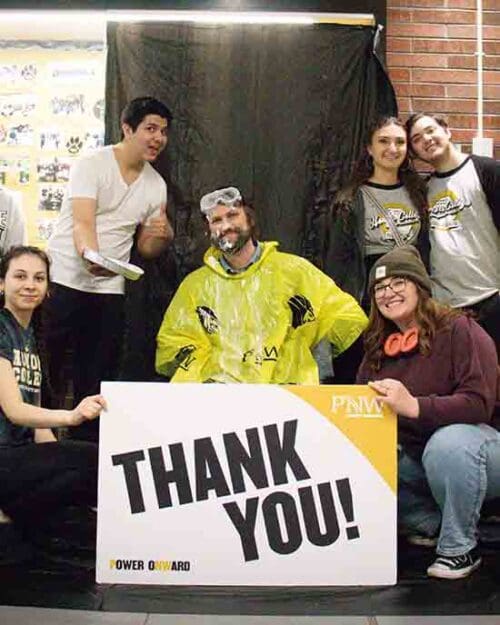 Six people pose together behind a PNW branded "Thank You" sign