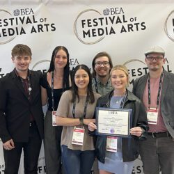 Five PNW communication students pose with studio technician Jake Giles. They are holding an award and standing in front of a "Festival of Media Arts" photo backdrop