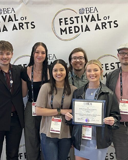 Five PNW communication students pose with studio technician Jake Giles. They are holding an award and standing in front of a "Festival of Media Arts" photo backdrop