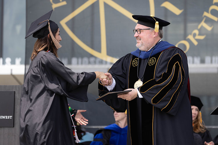 Chancellor Kenneth C. Holford stands on stage and hands a graduate their diploma while shaking their hand.