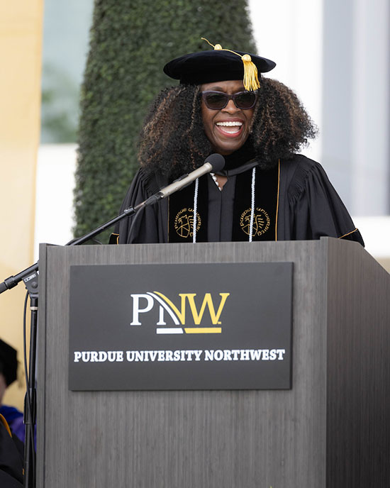 Regina Biddings-Muro stands in commencement regalia and speaks at a PNW branded podium