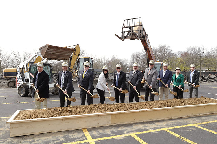 A group of people doing a ceremonial groundbreaking at PNW's Calumet Hall, using shovels to lift dirt from a box.