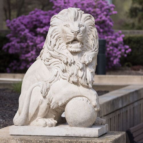 A PNW Lion statue with purple flowers blooming behind it