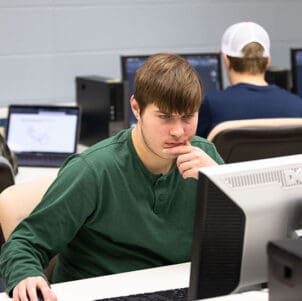 A student in a green long sleeve shirt works at a computer