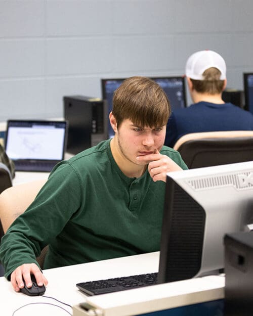 A student in a green long sleeve shirt works at a computer