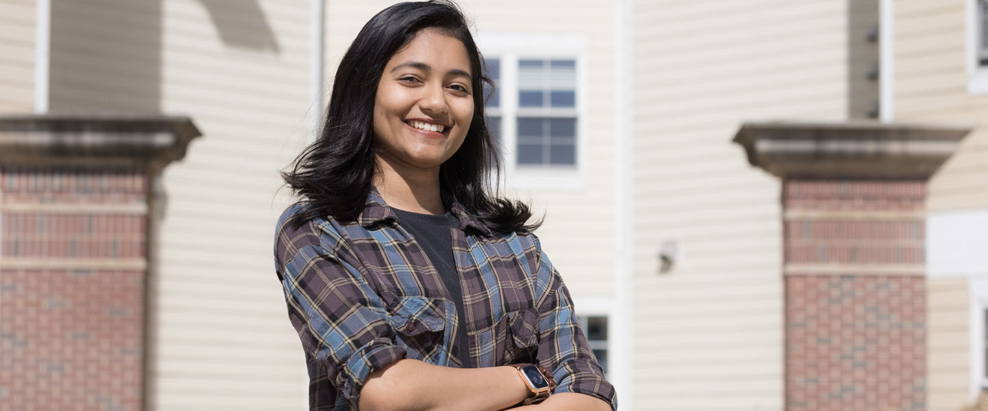 A student in plaid stands outside with their arms crossed