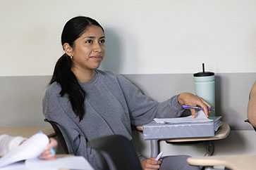 A student in a classroom wearing a gray hoodie