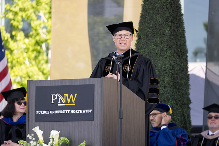 Joe Dudy stands at a PNW podium in commencement regalia.