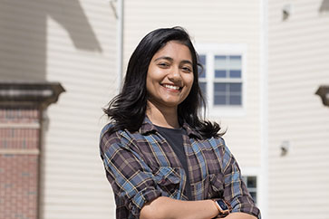 A student in plaid stands outside with their arms crossed
