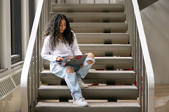 A student works with a laptop on a set of stairs