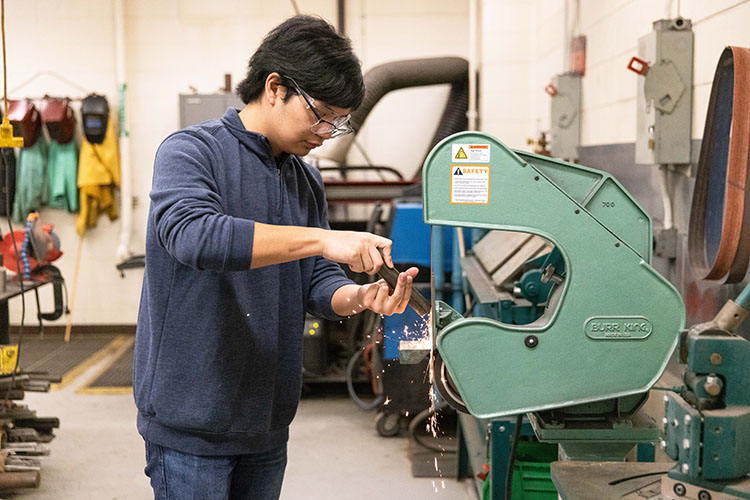 A student uses a belt grinder in a lab
