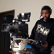 A studio in a PNW sweatshirt operates a camera in the production studio.