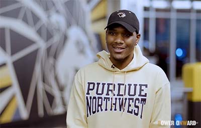 A student in Purdue Northwest gear sits in front of a lion mural