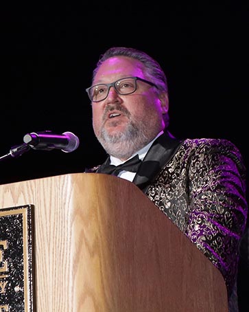 PNW Chancellor Holford in a spangled suit at a podium.
