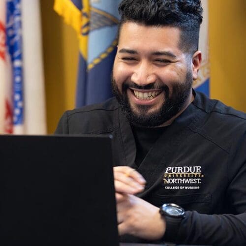 A PNW nursing student works on a laptop in front of flags