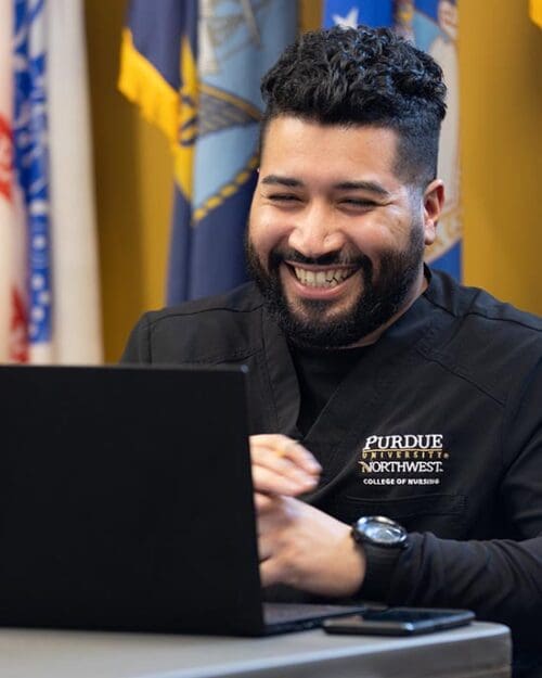 A PNW nursing student works on a laptop in front of flags