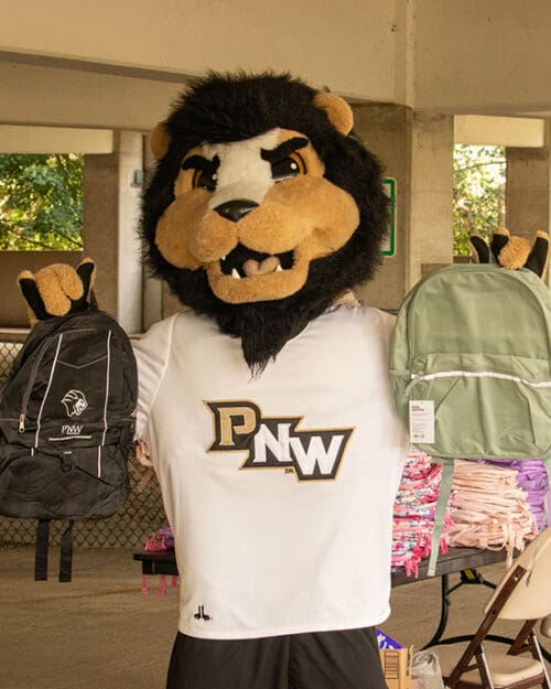 PNW Mascot Leo the Lion holds up two backpacks