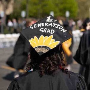 A student with a decorated mortarboard that reads "1st generation grad"