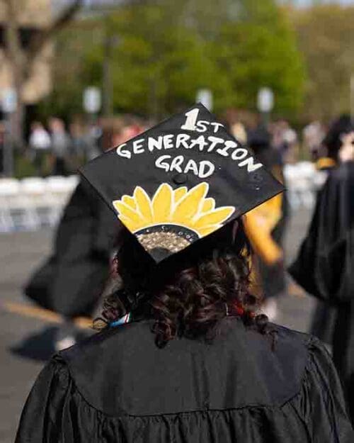 A student with a decorated mortarboard that reads "1st generation grad"